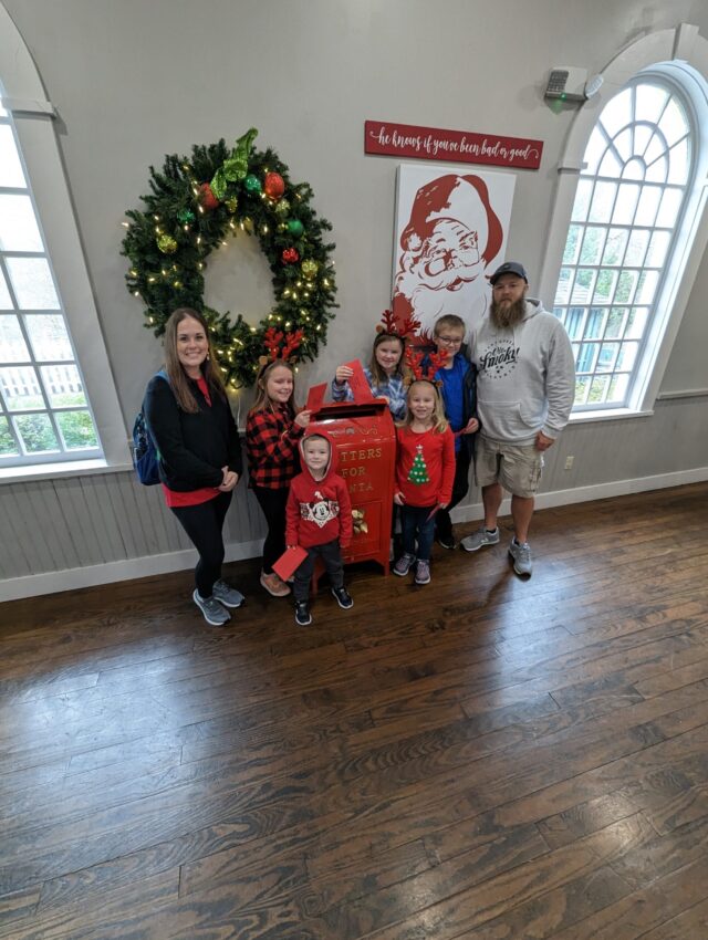 Dollywood Holiday Rope Drop Plan 1 family posing in santas workshop with a wreath at dollywood Photo Credit: Lindsay Harvey-Simply Touring