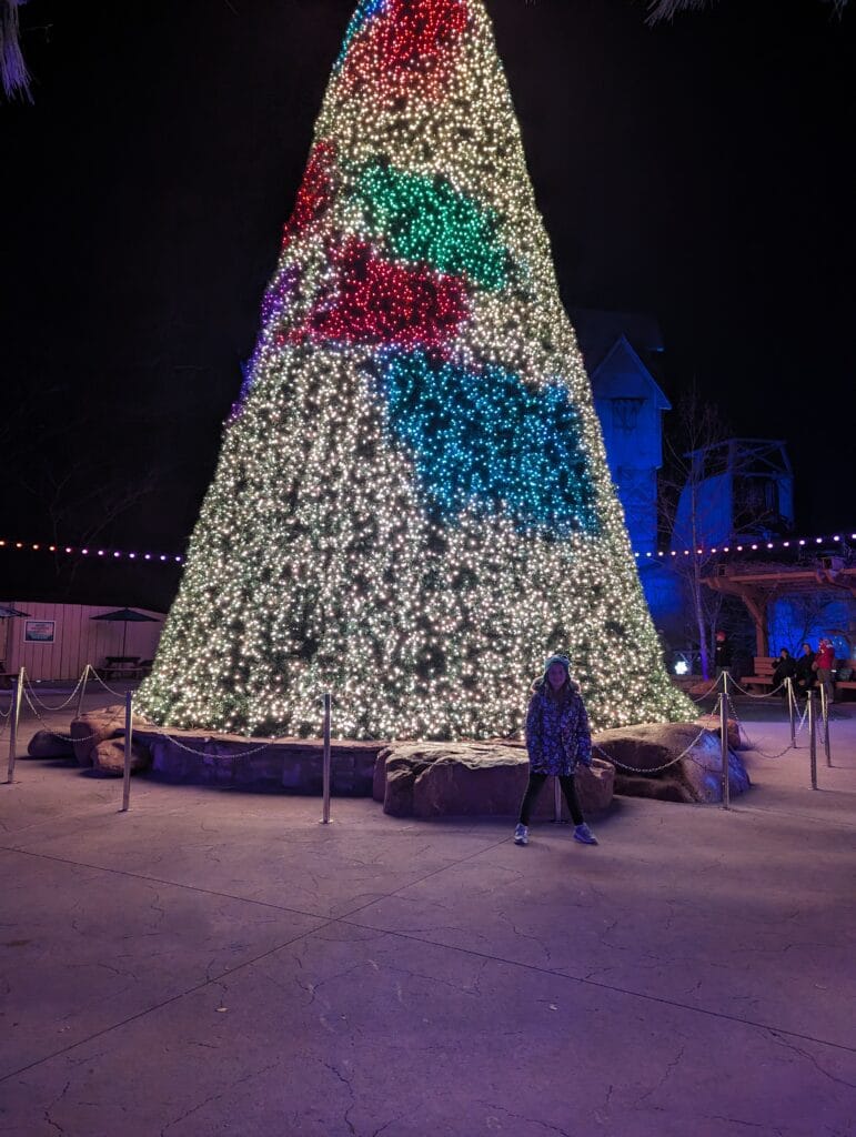Child in front of big lit tree at Dollywood during Smoky Mountain Christmas Festival Photo Credit: Lindsay Harvey-Simply Touring